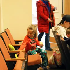 Child in pajamas sets a stuffed animals of the Grinch into a movie theater seat.