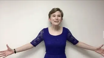 Person wearing a blue lace dress with arms extended wide against a plain white wall.