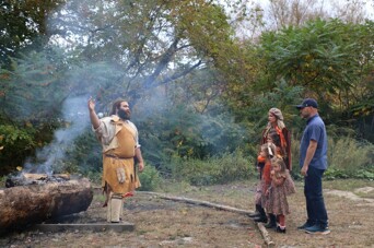 Family speaks with Educator standing before a burning mishoon on the Historic Patuxet Homesite.