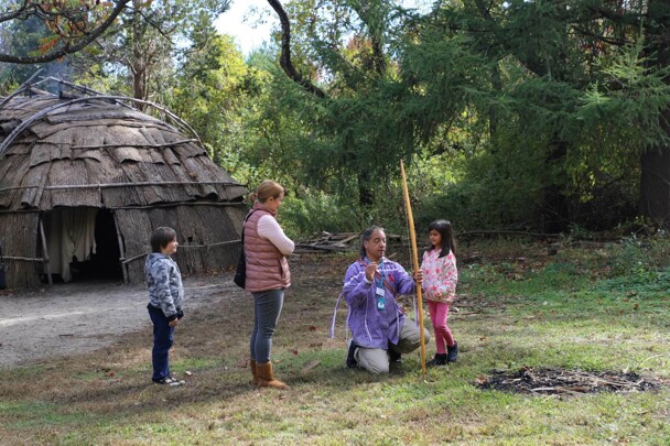 An Educator on the Historic Patuxet Homesite teaches young guests archery beside the winter wetu.