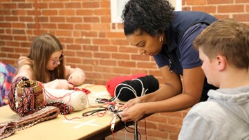 Educator demonstrates finger weaving to young learners.