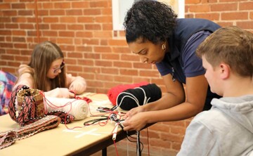 Educator demonstrates finger weaving to young learners.