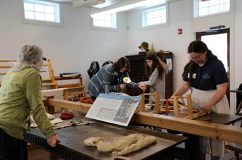 Museum educators teach young girl and her grandmother about making textiles by hand.