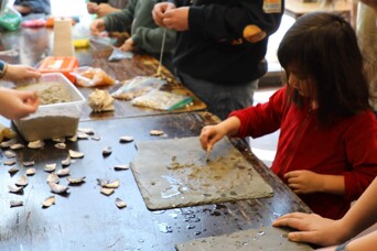 Young learner at a craft table makes art with clay and pieces of wampum.