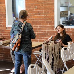 Educator pauses in finger weaving work to engage with an adult learner.