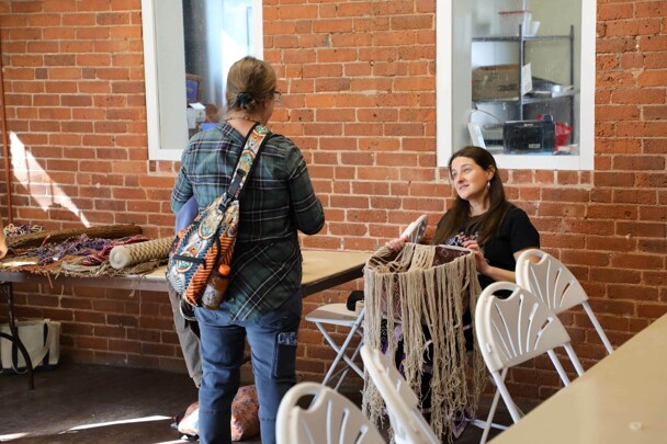 Educator pauses in finger weaving work to engage with an adult learner.