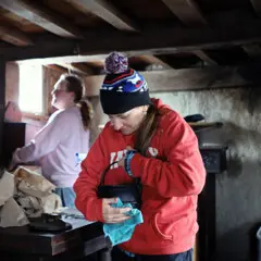 A volunteer in a red sweatshirt and winter hat holds a black pot that she is polishing inside a Pilgrim House.
