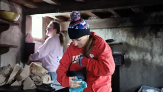 A volunteer in a red sweatshirt and winter hat holds a black pot that she is polishing inside a Pilgrim House.