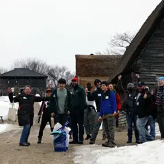 A group of volunteers standing in the English Village smile and wave.