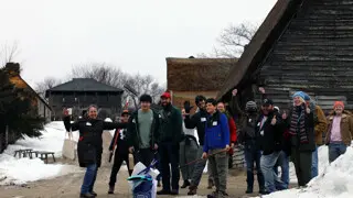A group of volunteers standing in the English Village smile and wave.