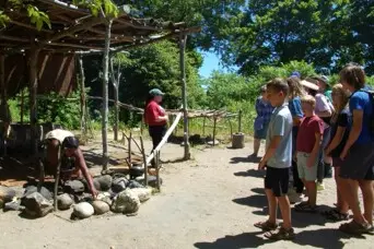 Guests gather as a Museum educator dressed in regalia cooks seasonal Wampanog food at the Cooking Arbor.