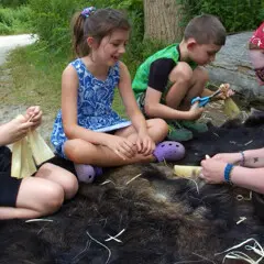 Museum educator teaches young guests how to make a cornhusk doll on the Historic Patuxet Homesite