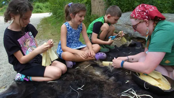 Museum educator teaches young guests how to make a cornhusk doll on the Historic Patuxet Homesite