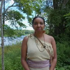 Museum Educator dressed in Wampanoag regalia surrounded by greenery