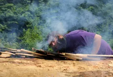 Museum Educator blows onto embers on mishoon to encourage the first burn on the log.