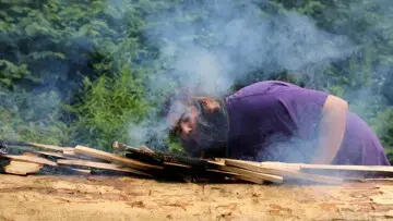 Museum Educator blows onto embers on mishoon to encourage the first burn on the log.