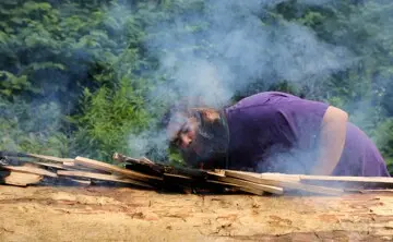 Museum Educator blows onto embers on mishoon to encourage the first burn on the log.