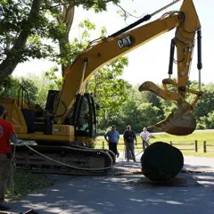 Yellow crane is poised to pickup 35 foot log as museum workers stand ready to assit