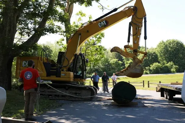 Yellow crane is poised to pickup 35 foot log as museum workers stand ready to assit