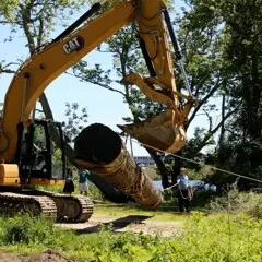 Large, yellow crane, picks up mishoon log for placement on the Historic Patuxet Homesite.