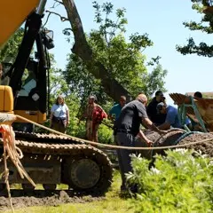 Museum workers gather around placed log on Historic Patuxet Homesite, with the crane still present.