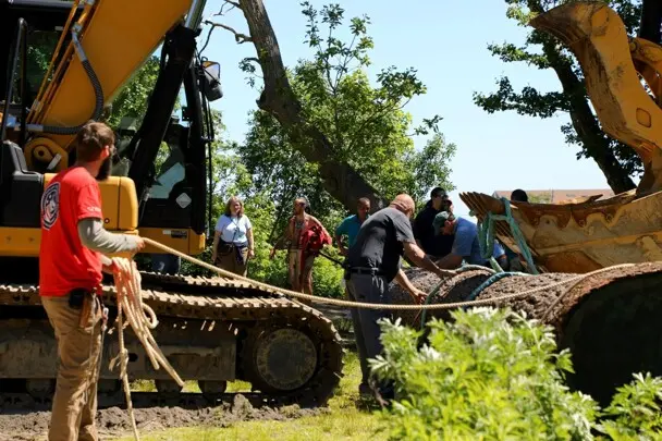 Museum workers gather around placed log on Historic Patuxet Homesite, with the crane still present.