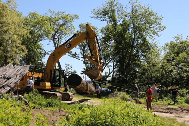 Museum worker uses rope to assist yellow crane as it places log for mishoon on the Historic Patuxet Homesite.