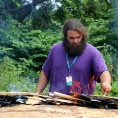 Museum Educator carefully tends to the fire on the mishoon.