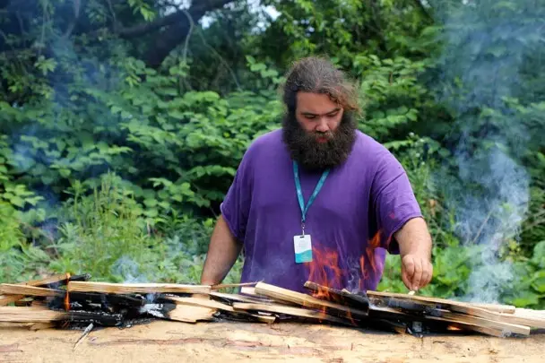 Museum Educator carefully tends to the fire on the mishoon.