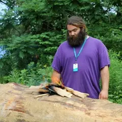 Museum Educator looks at small flame that is the first burn on the mishoon log.