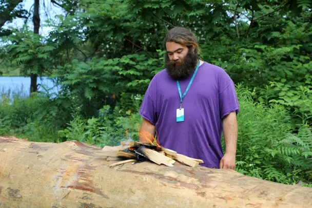 Museum Educator looks at small flame that is the first burn on the mishoon log.