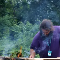 Museum educator carefully tends to the fire on the mishoon.