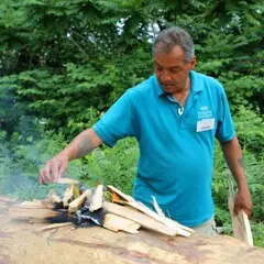 Museum Educator places wood cuttings on mishoon burn.