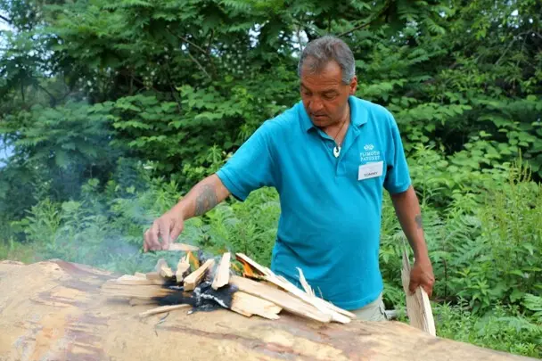 Museum Educator places wood cuttings on mishoon burn.