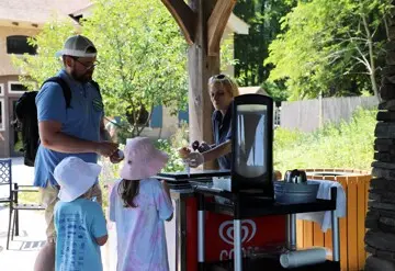 Cafe worker hands an ice cream cone to a young girl at an ice cream cart with her family.