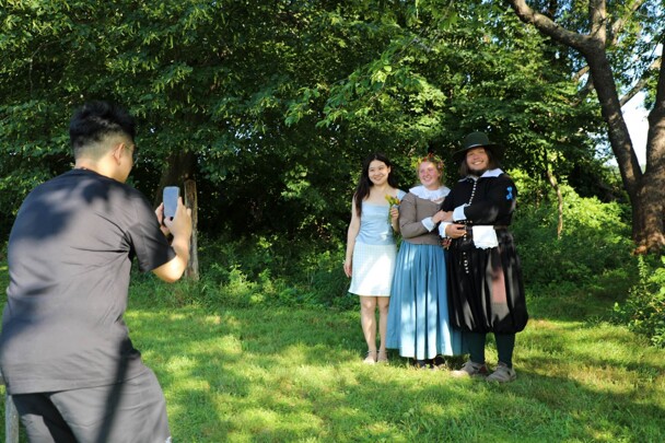 Museum guest poses with the Pilgrim couple as someone takes their photo.