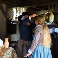 Pilgrim woman places flower crown ontop of Bride's head.