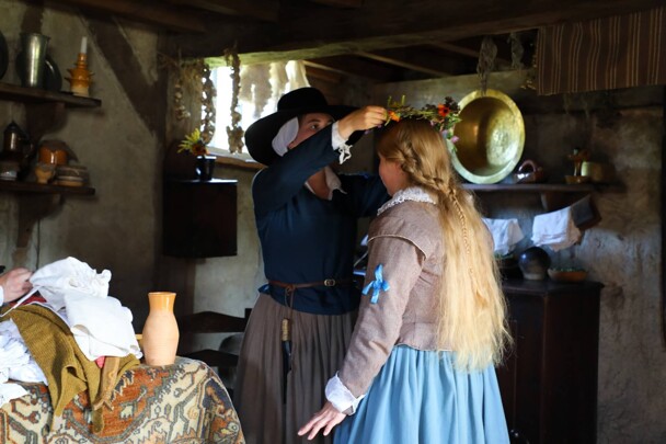 Pilgrim woman places flower crown ontop of Bride's head.