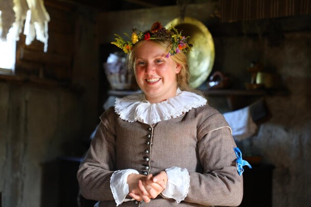 Pilgrim bride smiles inside house while wearing flower crown.