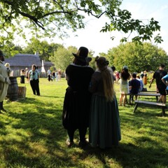 Pilgrim bride and groom stand close to each other while watching wedding guests celebrate on the Village Green.