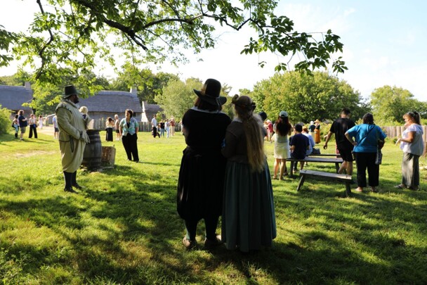 Pilgrim bride and groom stand close to each other while watching wedding guests celebrate on the Village Green.