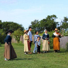 Guests mingle with Pilgrim women who hold musical instruments.