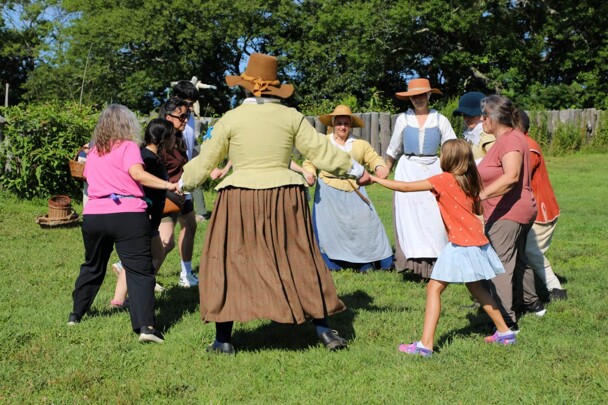 Pilgrims and Museum guests join hands and dance in a circle on the Village Green.
