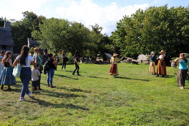 Guests watch three Pilgrim women as they entertain visitors with musical instruments.