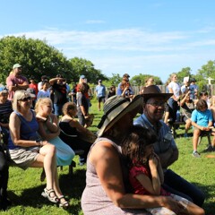 Museum guests gather as guests of a Pilgrim wedding on the Village Green. Most are seated, some stand.
