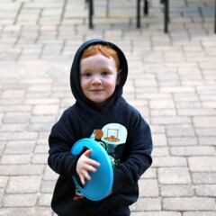 A young boy wears a dark hoodie and grasps a catcher for lawn games.