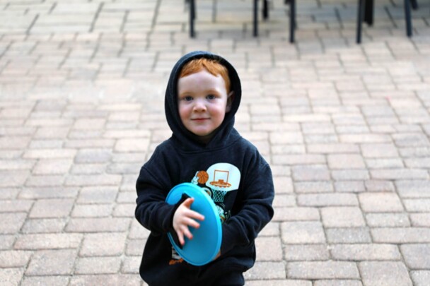 A young boy wears a dark hoodie and grasps a catcher for lawn games.