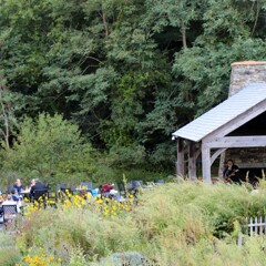 The Craft Center Pavillion with The GroovaLottos and seated audience beyond lush green gardens.