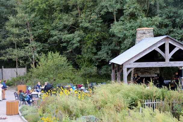 The Craft Center Pavillion with The GroovaLottos and seated audience beyond lush green gardens.