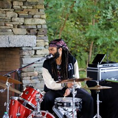 A member of The GroovaLottos plays the drums while singing into a microphone.
